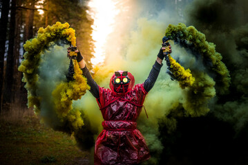 Person in red costume standing in the forest in the middle of colored smoke
