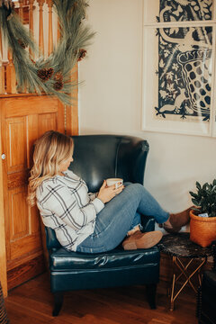 Side view of blonde woman sits on armchair and drinks coffee