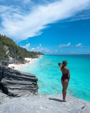 Woman in black bikini standing on rock near body of water