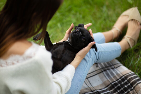 Woman in white long sleeve shirt and blue denim jeans holding black pug 'brussels griffon'
