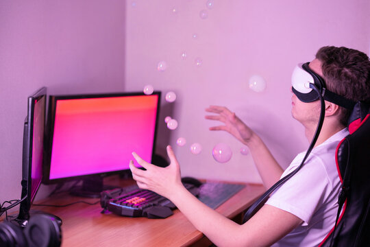 Young man wearing virtual headset sitting at a desk with two computer monitors