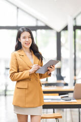 Plakat Successful Business Asian woman in Stylish Dress Using Tablet Computer, Standing in Modern Office Working on Financial, Business and Marketing Projects. Portrait of Beautiful Asian Manager.