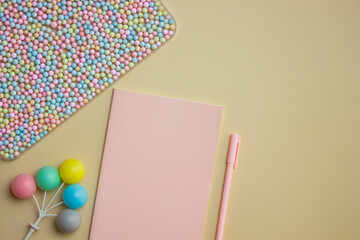 Colorful small balls with pink notebook and pen over the brown background. 