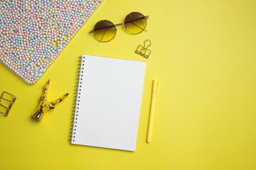 White notebook with sunglasses, pencil and colorful balls over the yellow background. 