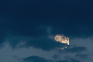 Naklejka na ściany i meble Growing moon in clouds on evening sky