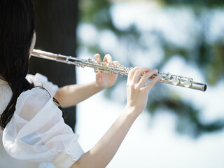 外で練習する女性フルート奏者の後ろ姿と手元