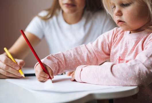 Little girl toddler with her mother drawing with colored pencils on table in children's room at home