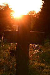 Kreuz als Grabstein auf einem Friedhof bei Sonnenuntergang im Gegenlicht
