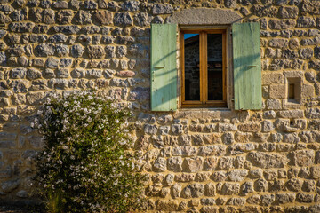 Old house stone facade with a window with green shutters in Boucieu Le Roi in Ardeche (France)