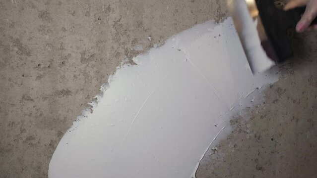 Puttying process. A female gloved hand works with a concrete wall. White putty lays evenly on the surface of the wall