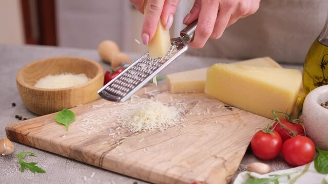 woman grates piece of parmesan hard cheese on a grater at domestic kitchen
