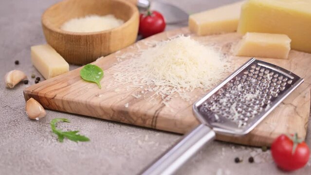 Pieces of parmesan hard cheese and grated cheese on a wooden cutting board at domestic kitchen