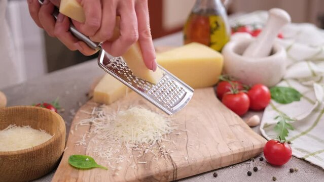 woman grates piece of parmesan hard cheese on a grater at domestic kitchen