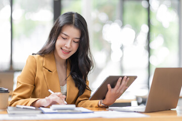 Asian businesswoman working in the  workplace Office, Her is using touchpad while reading an e-mail on laptop and taking notes on the paper, accounting, tax, Financial, Business concept