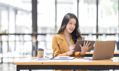 Asian businesswoman working in the  workplace Office, Her is using touchpad while reading an e-mail on laptop and taking notes on the paper, accounting, tax, Financial, Business concept