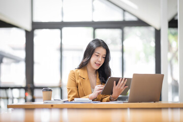 Asian businesswoman working in the  workplace Office, Her is using touchpad while reading an e-mail on laptop and taking notes on the paper, accounting, tax, Financial, Business concept