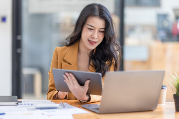 Asian businesswoman working in the  workplace Office, Her is using touchpad while reading an e-mail on laptop and taking notes on the paper, accounting, tax, Financial, Business concept