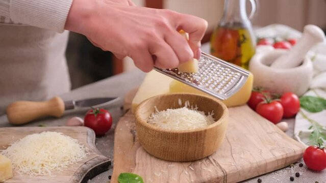 woman grates piece of parmesan hard cheese on a grater at domestic kitchen