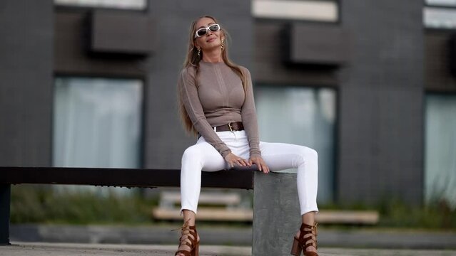 Beautiful playful blonde woman is sitting on bench in city seductively, sexuality and femininity