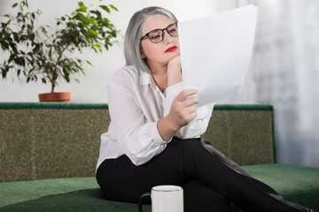 Portrait of an adult woman entrepreneur with grayish hair in a managerial position, dressed in a white blouse and busy working in the office
