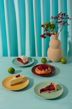 Vertical high angle still life studio shot of delicious cakes, pies, limes and vase with flowers and viburnum against blue background