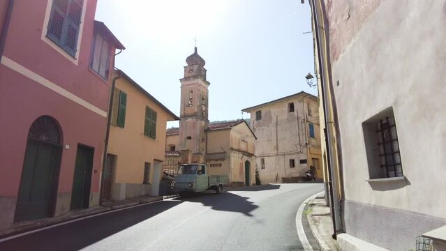 Old street in Italian Mountain village in Liguria. Piaggiop Ape standing infront of old church building with blue sky and vivid colors.