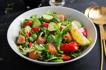 Ketogenic salad with salted salmon fish, lemon, cucumber, olives, tomatoes, green lettuce salad and honey mustard dressing. Healthy food trend.
