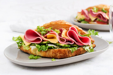 Fresh croissant or sandwich with salad, ham and cheese on light  background.