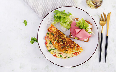 Omelette with tomatoes, cheese, green onion and sandwich with ham on white plate.  Frittata - italian omelet. Top view