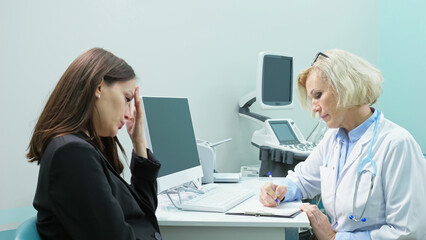 Careful female doctor writes prescription listening to symptoms of dejected woman. Lady patient complains of migraine and strong headache in ultrasound room