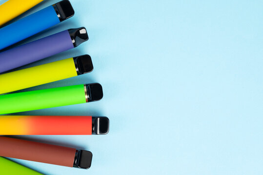 Layout of colorful disposable electronic cigarettes with shadows on a blue background. The concept of modern smoking, vaping and nicotine. Top view