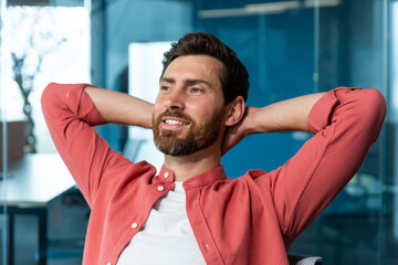 Fototapeta premium Young successful businessman startuper rests in office, man in red shirt throws hands behind head and dreams visualizes, designer thinks about new project.