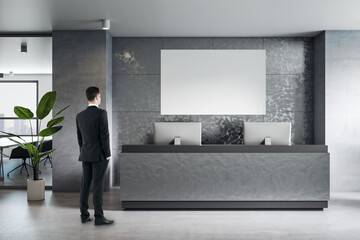 Businessman back view looking at blank white poster with space for your logo or text on grey wall...