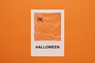 From above view shot of decorative toy spider with web in white frame with Halloween text printed on it, orange background