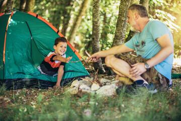 Naklejka na ściany i meble Father and son spending happy leisure time together outdoors in forest trees background.