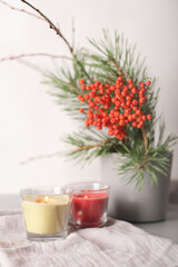 rowanberry and pine branch in a concrete vase and glowing candles on grey background. blog autumn content. thanksgiving home decor, vertcal