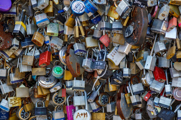 Old and new padlocks with names and dates written on them lock on a bridge as a sign of love in San...