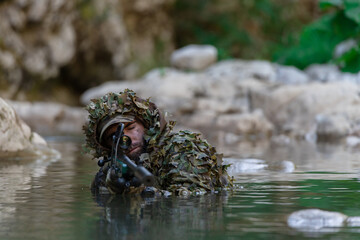A military man or airsoft player in a camouflage suit sneaking the river and aims from a sniper...