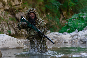A military man or airsoft player in a camouflage suit sneaking the river and aims from a sniper...
