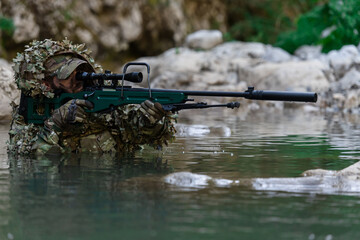A military man or airsoft player in a camouflage suit sneaking the river and aims from a sniper...