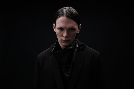 Horizontal medium studio portrait of stylish Caucasian man wearing dark fashionable clothes standing against black background