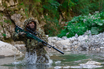 A military man or airsoft player in a camouflage suit sneaking the river and aims from a sniper...