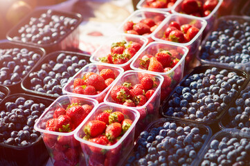 Strawberries and blueberries on a farmer's market stall on a sunny day. Fresh berries are laid out in even rows. Healthy food concept