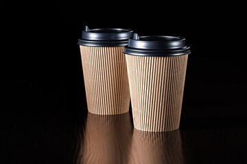 A pair of paper cups for hot coffee, tea, drinks with black lids on a black background. Side view.