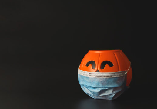 plastic halloween pumpkin wearing medical face mask  on black background with copy space. New normal  halloween concept