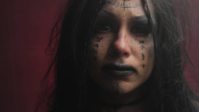 Portrait of a witch girl with black eyes on a red background in the smoke.