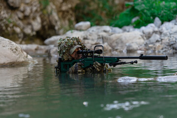 A military man or airsoft player in a camouflage suit sneaking the river and aims from a sniper...