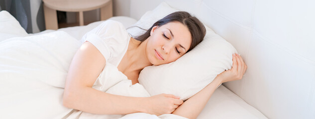View an attractive young woman sleeping well in bed hugging soft white pillow. Caucasian girl...