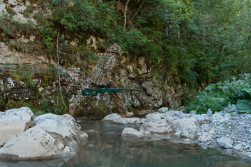 A military man or airsoft player in a camouflage suit sneaking the river and aims from a sniper...