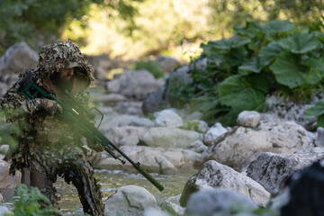 A military man or airsoft player in a camouflage suit sneaking the river and aims from a sniper...